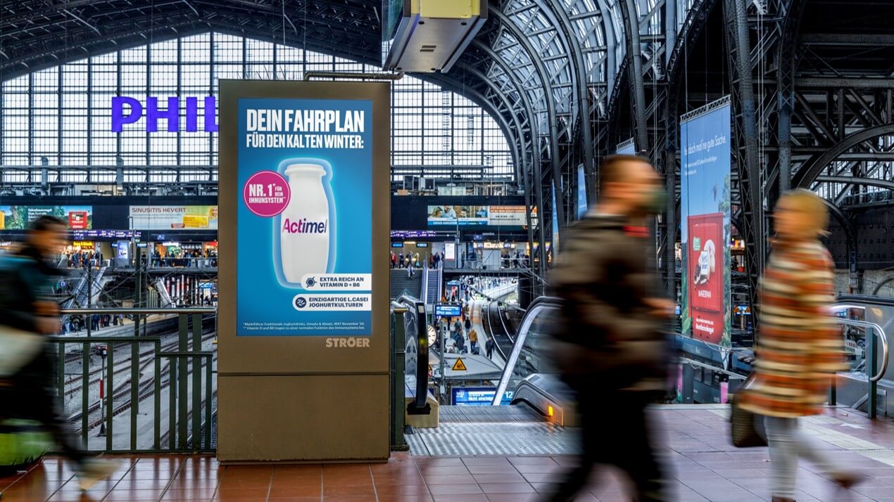 PV Station mit Actimel-Werbung im Hauptbahnhof vor großem Fahrgastaufkommen, betont Immunstärkung und Wintervorbereitung