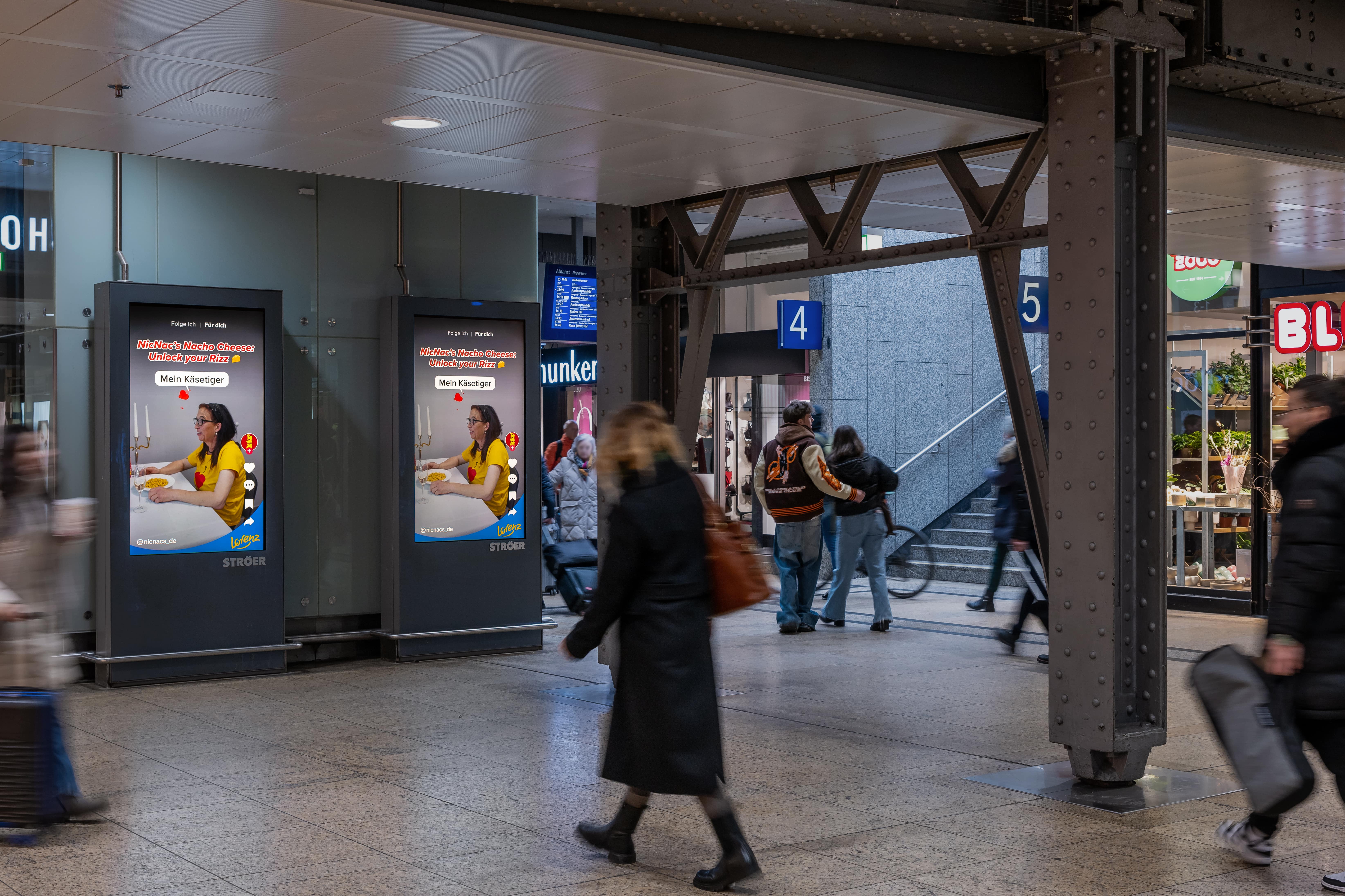 Auf Digital-Out-of-Home verlängerte Werbung mit Käse-Prinzessin auf zwei digitalen Screens in Bahnhofspassage mit hohem Passantenaufkommen