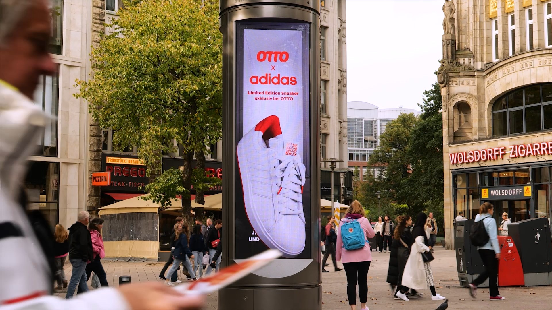 **Alt-Tag:** Digitaler City Tower in Hamburg zeigt einen 3D-Spot des exklusiven OTTO x adidas Sneakers, umgeben von Passanten in belebter Einkaufsstraße.