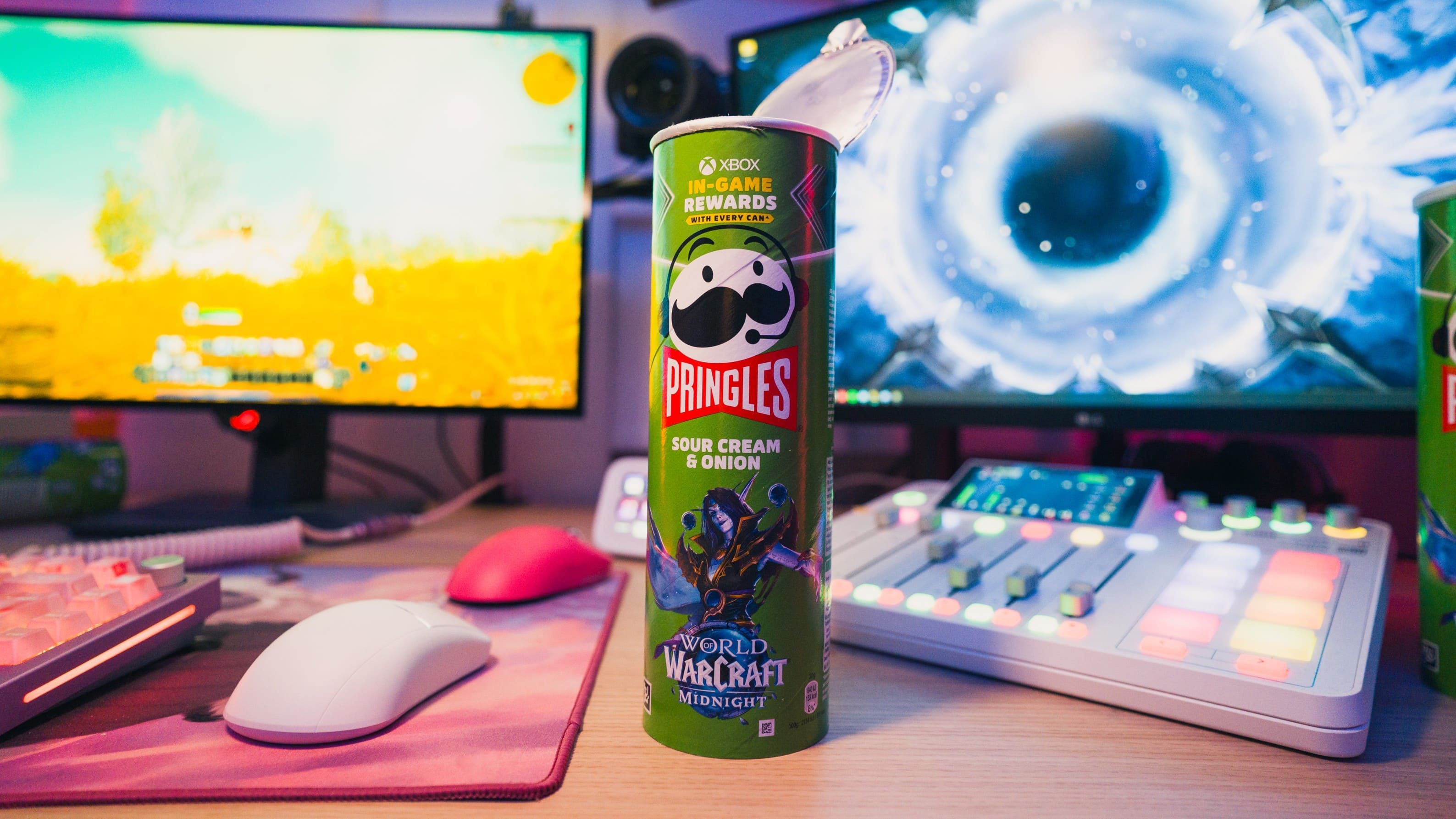 Nahaufnahme einer geöffneten Pringles-Dose der Sorte „Sour Cream & Onion“ im Design des Videospiels „World of Warcraft: Midnight“. Die Dose steht auf einem Schreibtisch vor zwei Gaming-Monitoren und einem Mischpult. Auf der Verpackung wird eine Xbox-Aktion mit dem Hinweis „In-Game Rewards with every Can“ beworben.