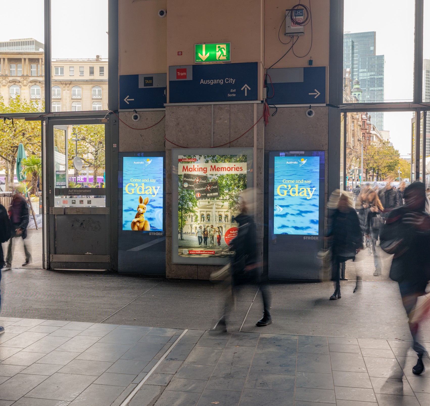 Connected-Ad-Kampagne von Tourism Australia mit mehreren digitalen Displays im urbanen Bahnhofsumfeld, Känguru-Motiv und hoher Passantenfrequenz.