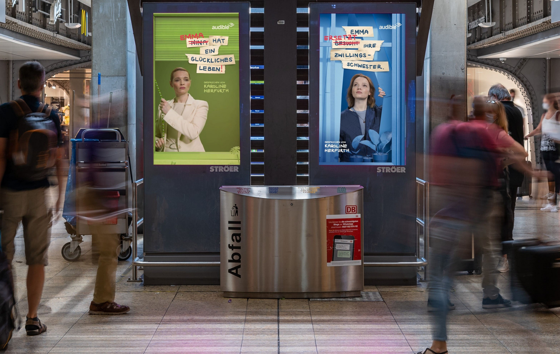 Digitale Screens von Ströer in einer Bahnhofshalle zeigen nebeneinander zwei Motive der Audible-Hörbuchkampagne mit Karoline Herfurth hinter einem Abfallbehälter.