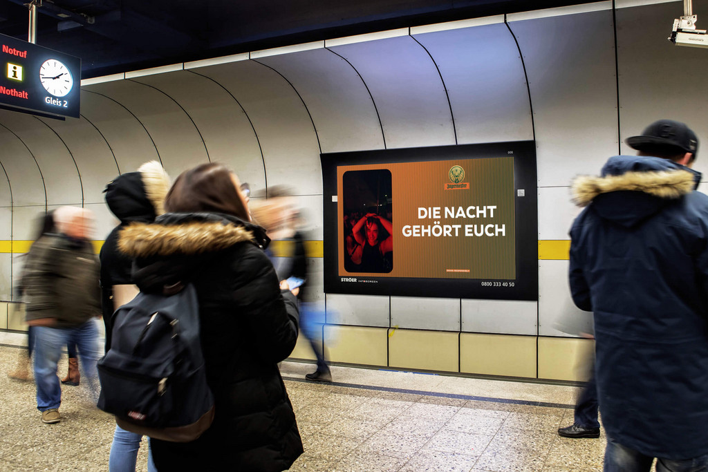 Digitale Out-of-Home-Werbefläche mit Werbung von Jägermeister in U-Bahnstation mit aufmerksamkeitsstarkem Motiv, platziert im Blickfeld wartender Passanten im urbanen Umfeld.